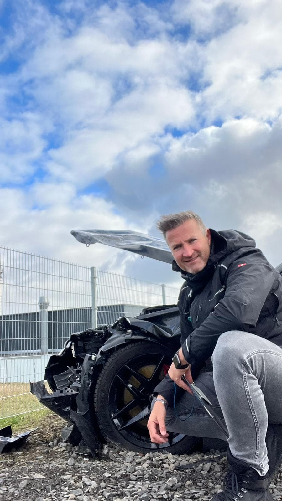 Sebastian Paul begutachtet den Frontschaden eines schwarzen Sportwagens nach einem Unfall